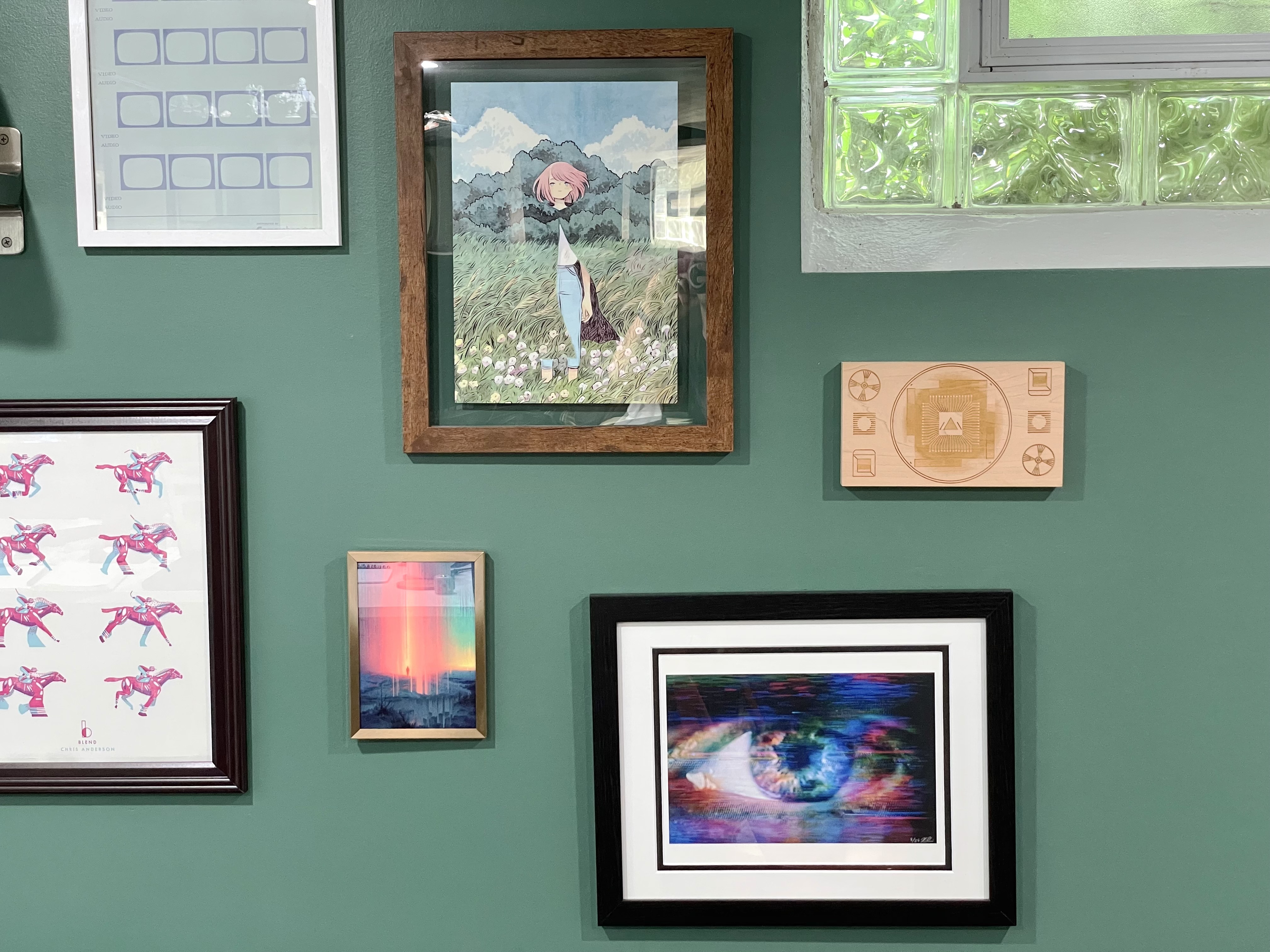 Framed watercolor print, two glitch prints, and a wood engraving on a green wall